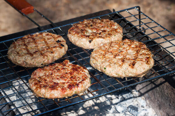 4 Burger-Patties auf einem Grillrost