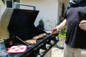Mann grillt auf dem Gasgrill saftige Steaks, während im Hintergrund eine Abdeckung für seinen Gasgrill steht